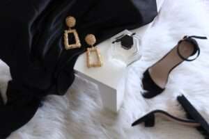 Golden rectangular earrings, a flask of perfume, and black high heeled shoes